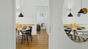 Un comedor moderno con un espejo redondo, lámparas colgantes negras y suelo de madera.