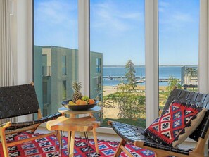 Un balcon avec deux chaises, une petite table sur laquelle sont disposés des fruits, et une vue sur la mer et les bâtiments.