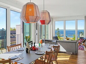 Ein Essbereich mit Tisch für vier Personen, große Fenster mit Meerblick und ein Balkon mit Sitzgelegenheit im Freien.