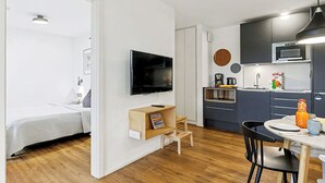 Un apartamento moderno con suelo de madera, cama, televisor, kitchenette y comedor.