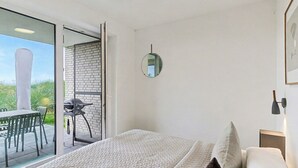 Un dormitorio con una cama grande, vistas al exterior, una pequeña mesa con sillas y una puerta al balcón.