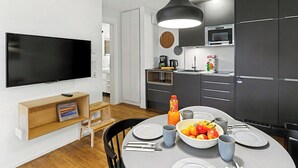 Una cocina moderna con armarios oscuros, un televisor grande y un comedor con una mesa lista para dos.
