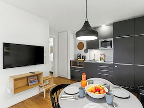 Una cocina moderna con armarios oscuros, un televisor grande y un comedor con una mesa lista para dos.