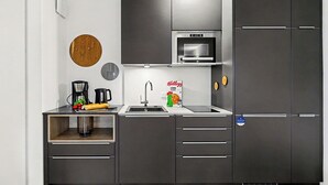 Una cocina moderna con armarios oscuros, un microondas de acero inoxidable, una tetera y una cafetera.