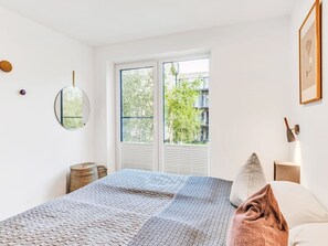 Ein Schlafzimmer mit einem Bett, einem Fenster, einem an der Wand befestigten Spiegel und einem gerahmten Bild.