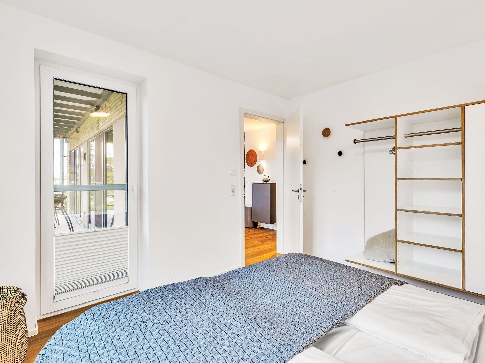 A bedroom with a bed, a wardrobe, a door leading to a balcony, and a wall-mounted light fixture.