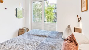 Een slaapkamer met een bed, een raam, een spiegel aan de muur en een ingelijste foto.