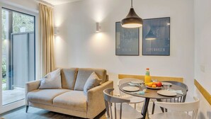 Un comedor moderno con una mesa redonda, sillas y un sofá. Hay cuadros enmarcados en la pared, una lámpara colgante y una ventana con cortinas.