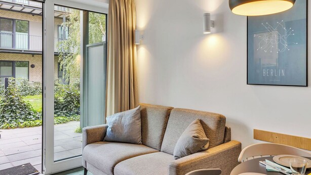 Una sala de estar moderna con un sofá, una mesa de comedor con sillas, un ventanal con cortinas y un cuadro enmarcado en la pared.