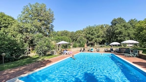Una piscina rectangular con agua azul cristalina, rodeada por un patio de ladrillo. Hay sillones reclinables y sombrillas para tomar el sol.