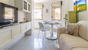 Un espacio habitable compacto con una televisión, una mesa de comedor, sillas, un sofá y un cuadro en la pared.