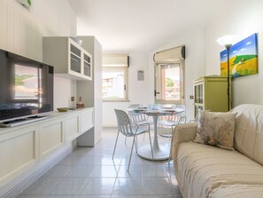 Ein gemütlicher Wohnbereich mit Fernseher, Esstisch, Stühlen, einer Couch und einem Bild an der Wand.