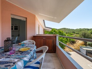 Ein Balkon mit Tisch für zwei Personen, einem Holzkasten und Blick auf grüne Hügel.