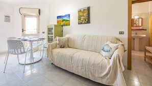 Una sala de estar con un sofá, una mesa de comedor con sillas y dos cuadros en la pared.