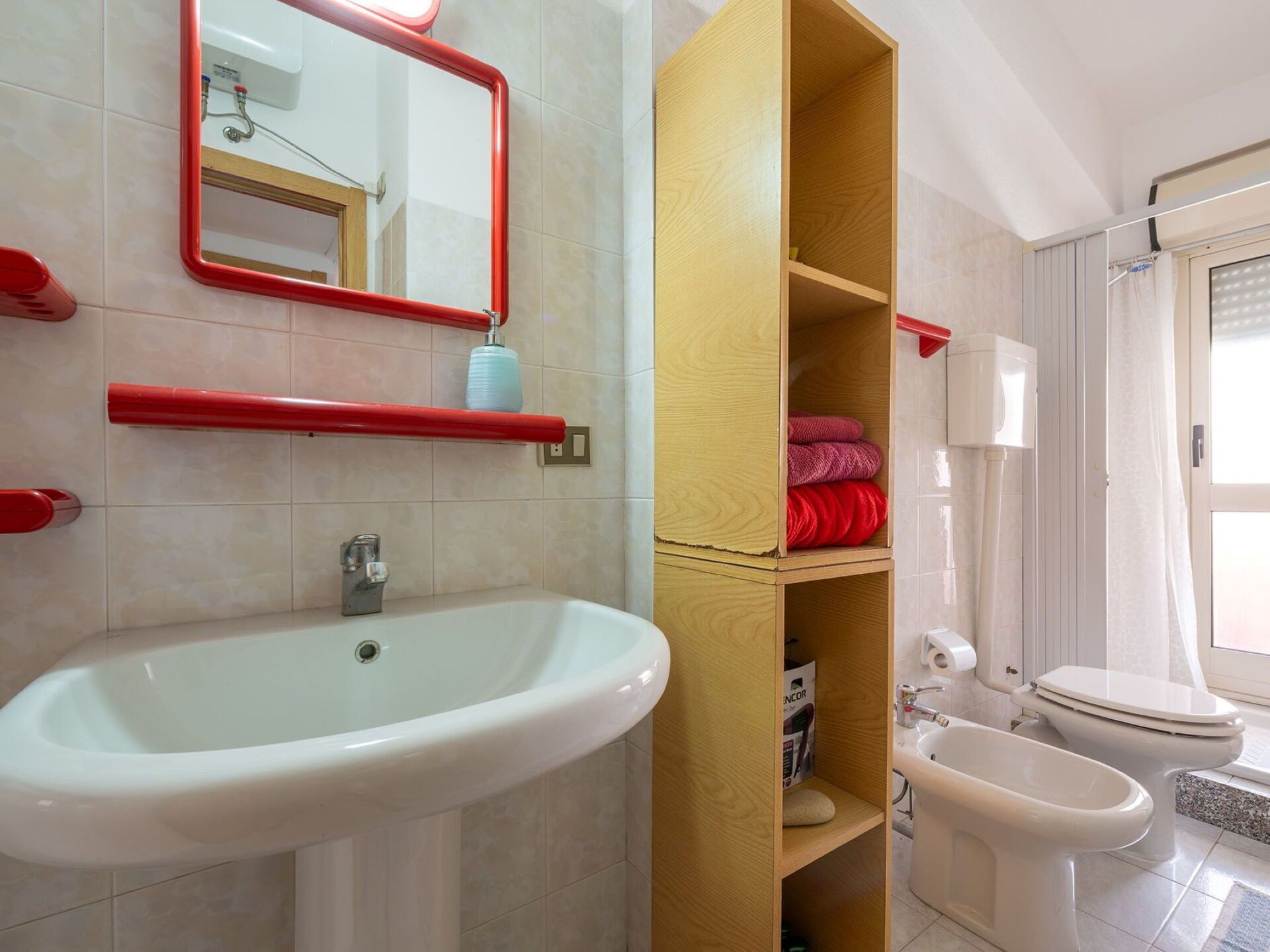 Une salle de bain équipée d’un lavabo, de toilettes, d’un bidet et d’une étagère en bois.