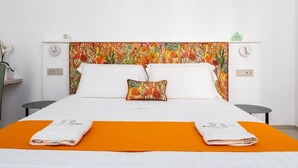 Une chambre d’hôtel avec un lit, deux tables de chevet, une petite table, un coussin décoratif et une couvre-lit orange.
