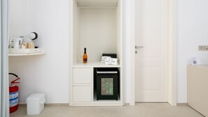 Una habitación blanca con una puerta, un estante pequeño con objetos y un electrodoméstico negro.