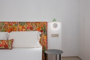 Una cama con un cabecero colorido, una mesita redonda y un enchufe de pared.