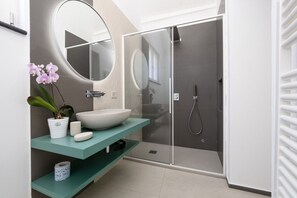 Ein modernes Badezimmer mit einem großen, ovalen Spiegel, einem weißen Waschbecken, einer Duschkabine und einer Waschtischunterschrank in Türkis.