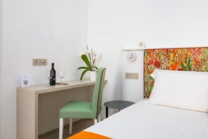 Ein Hotelzimmer mit einem Bett, einem Schreibtisch mit Stuhl, einem kleinen Tisch, einer Zimmerpflanze und einem dekorativen Kopfteil.