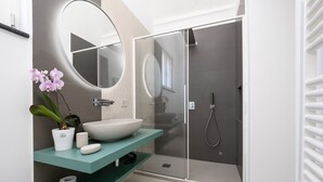 Un baño moderno con un espejo ovalado grande, un lavabo blanco, un box de ducha y un mueble de tocador color turquesa.