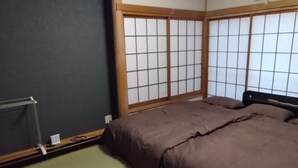 Una habitación tradicional japonesa con suelo de tatami, futón, puertas correderas shoji y ventilador de techo.