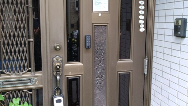 Una puerta marrón con cerradura electrónica, un cartelito encima y una ventana con diseño decorativo.