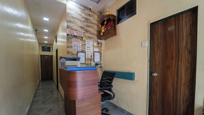 A reception area with a wooden reception desk, a black office chair, a wooden door, and a wall with various notices. - AAI OM Residency (Mumbai)
