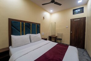 A hotel room with a bed, a nightstand, a chair, a wardrobe, and a ceiling fan. - AAI OM Residency (Mumbai)