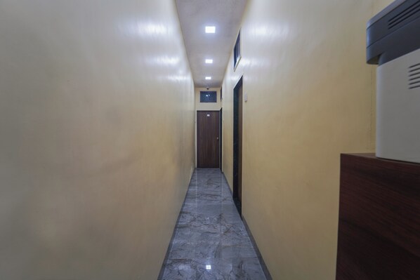 A narrow hallway with a marble floor, beige walls, and a wooden door at the end. - AAI OM Residency (Mumbai)