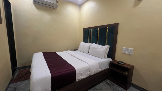 A hotel room with a bed, a bedside table, an air conditioning unit, and a power outlet. - AAI OM Residency (Mumbai)