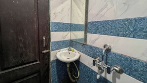 A bathroom with a marble sink, a mirror, and a shower area. - AAI OM Residency (Mumbai)