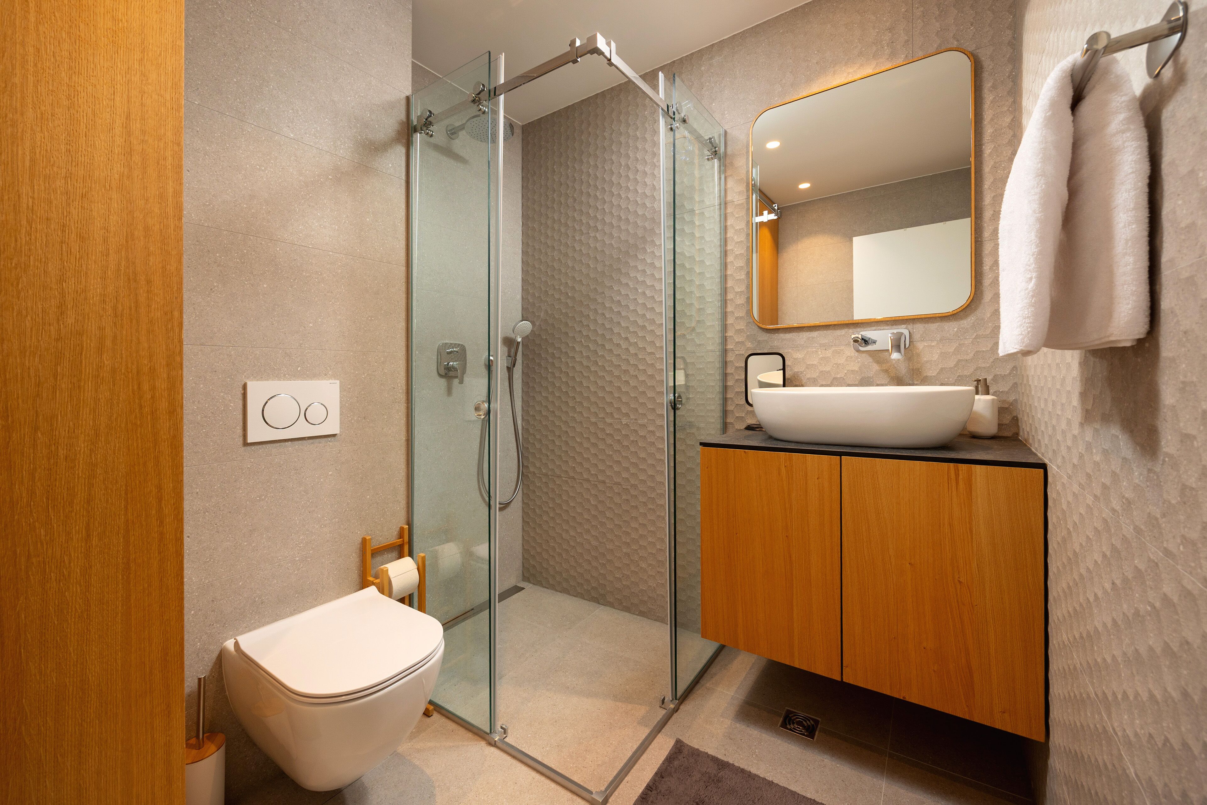 A modern bathroom with a glass-enclosed shower, a wooden vanity, and a large mirror.