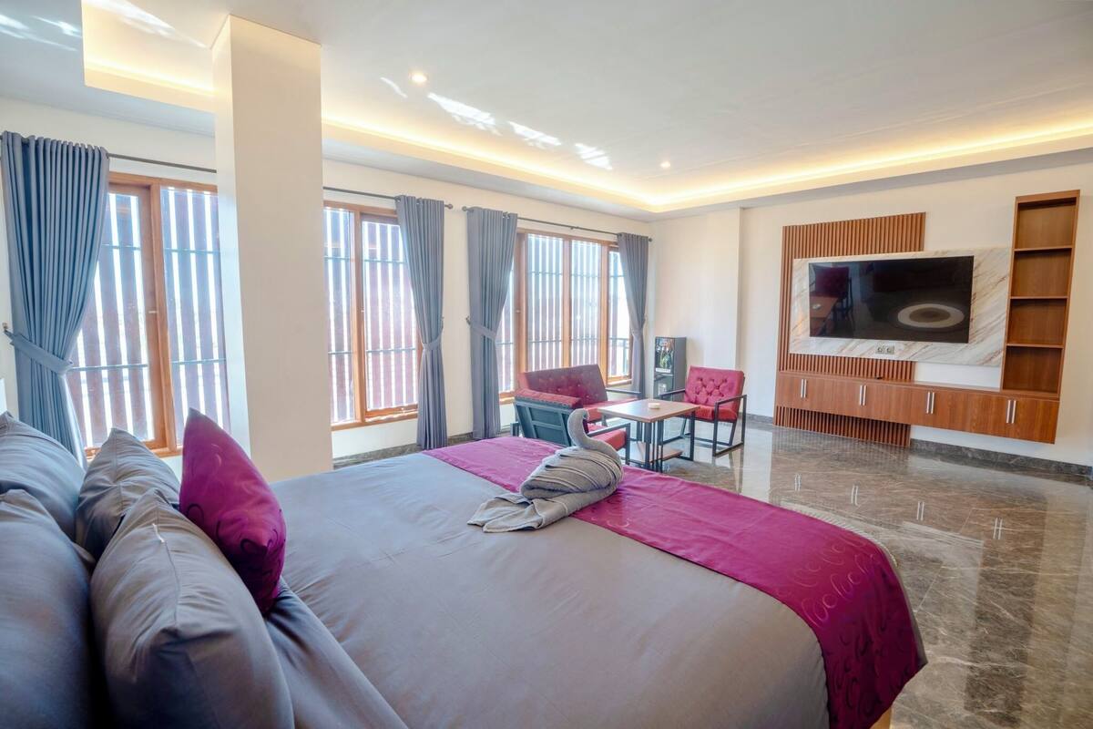 Une chambre d’hôtel avec un grand lit, un bureau avec une chaise, un téléviseur fixé au mur et une fenêtre avec des rideaux.
