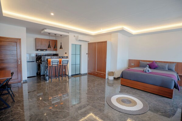 A modern bedroom with a large bed, a small kitchen area, and a dining space. - Kusuma Apartment Canggu (Tibubeneng)