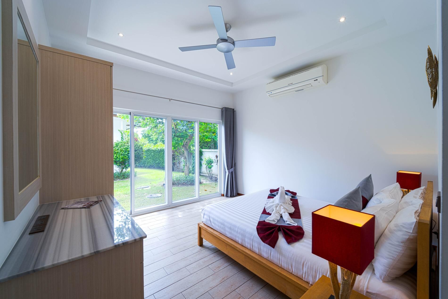 Une chambre moderne dotée d’un grand lit, d’un ventilateur de plafond, d’un appareil de climatisation et offrant une vue sur un jardin grâce à une porte coulissante.