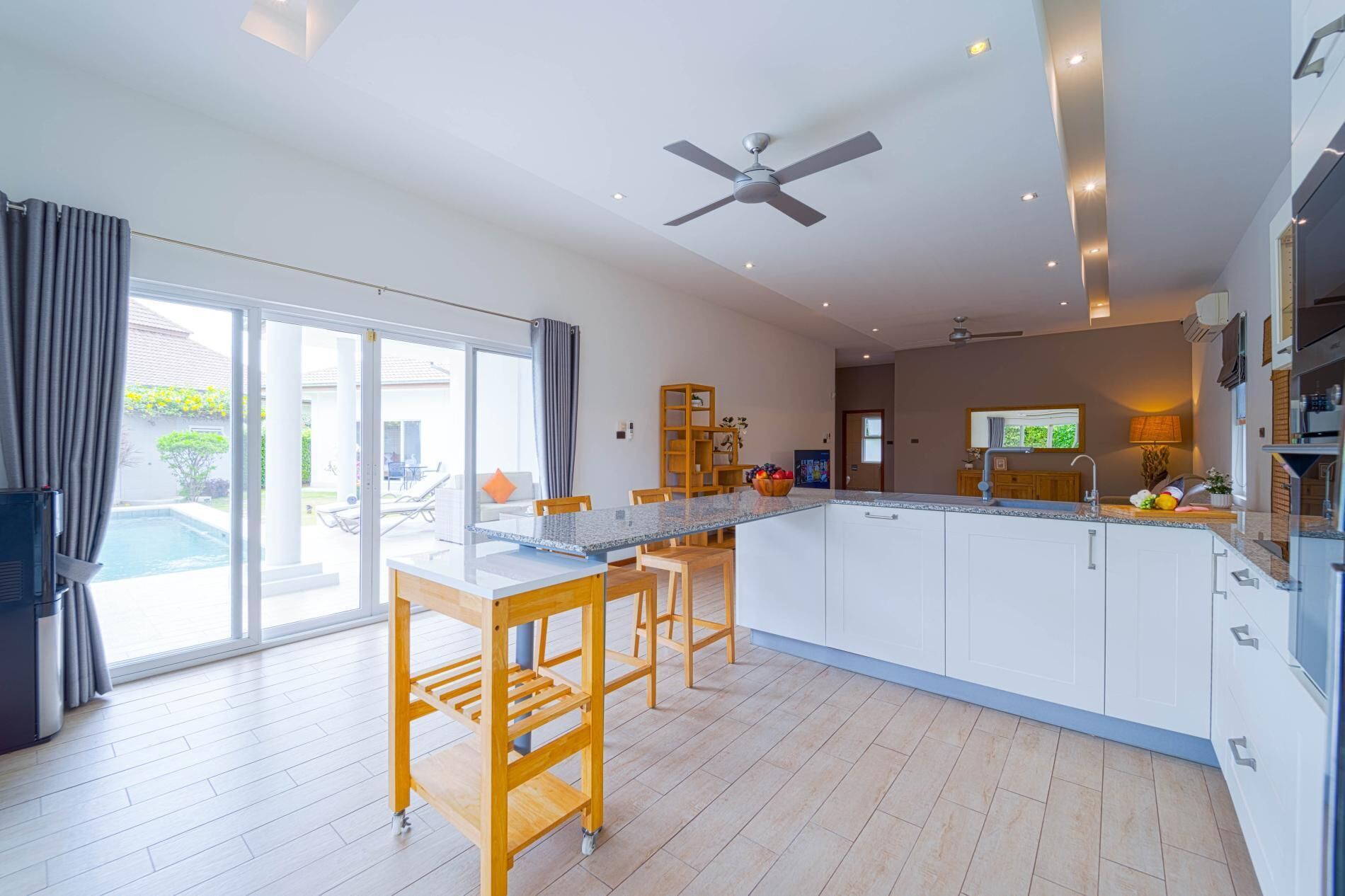 A modern kitchen with a central island, wooden chairs, and a ceiling fan.