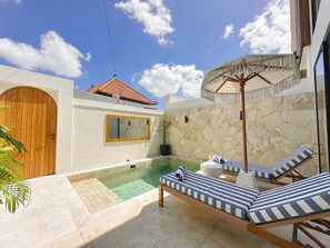 A poolside area with lounge chairs, a stone wall, and a wooden door. - Villa Sylvia Canggu (Canggu)
