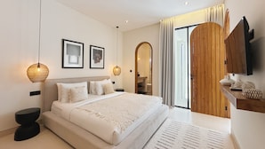 A modern bedroom with a large bed, bedside lamps, and a wooden door leading to a bathroom. - Villa Sylvia Canggu (Canggu)