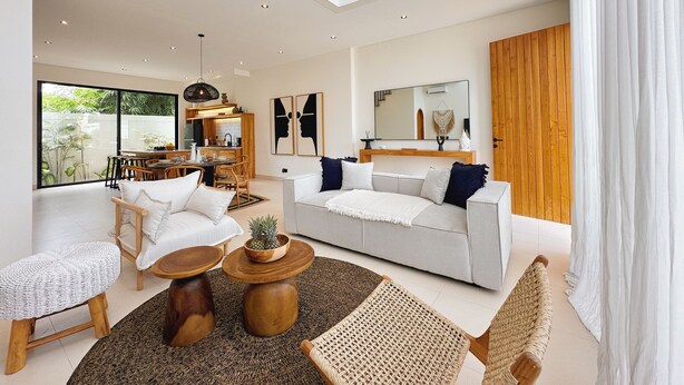 A spacious living area with a large sofa, a dining table, and a kitchen in the background. - Villa Sylvia Canggu (Canggu)