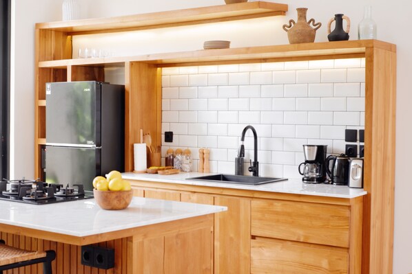 Une cuisine moderne avec des meubles en bois, un plan de travail blanc, un réfrigérateur noir, un évier et une machine à café.