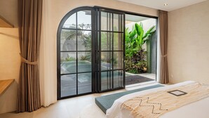 Een moderne slaapkamer met een grote schuifdeur naar een zwembad, een bed met een beige deken, en uitzicht op groen.