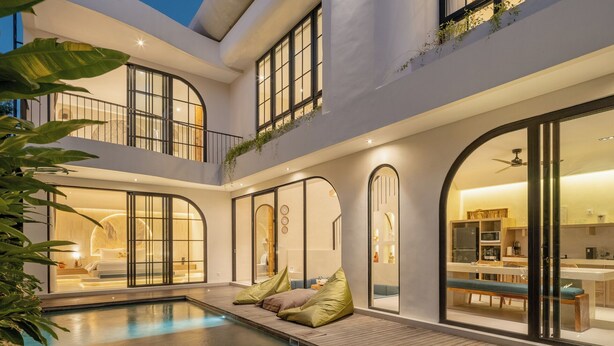 Een modern huis met een zwembad, grote ramen en een balkon met planten.