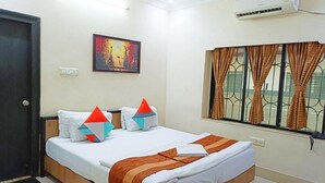 Une chambre d’hôtel avec un lit, un tableau au mur, un appareil de climatisation et une fenêtre avec des rideaux.