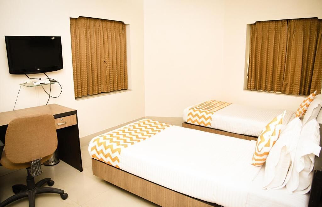 Habitación de hotel con dos camas, un escritorio, una silla, un televisor y cortinas.