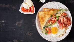 Une assiette de petit-déjeuner avec des toasts, un œuf, du bacon, des tomates et des jeunes pousses, le tout présenté sur une assiette à motifs.