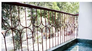Un balcon doté d’une balustrade en métal, donnant sur une rue animée par la circulation des voitures et bordée de verdure.