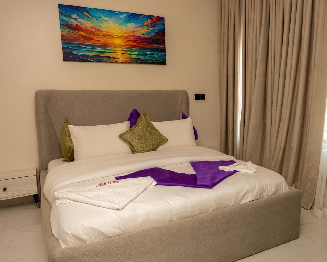 A bedroom with a bed, a nightstand, a painting, and a window with curtains.