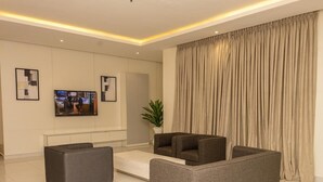 A modern living room with a flat-screen TV, two sofas, a coffee table, and a large window with curtains.