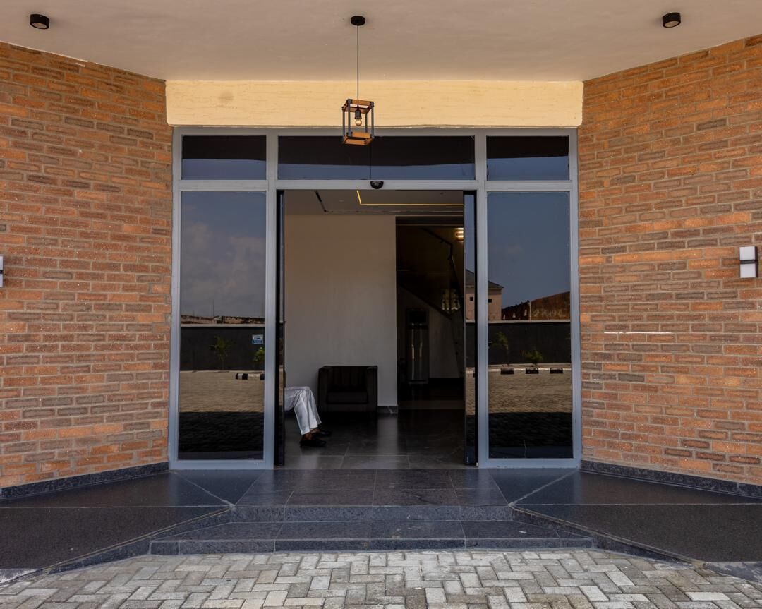 A building entrance with a brick facade, large glass doors, and a tiled floor.